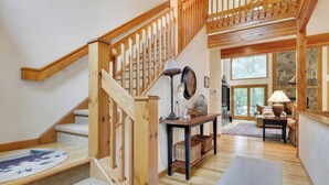 Eine Holztreppe mit Geländer, ein Konsolentisch mit Dekoration und Blick auf einen Außenbereich durch ein großes Fenster.