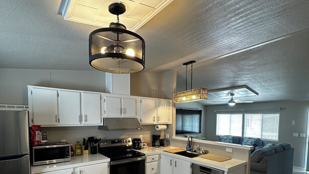 Una cocina moderna con armarios blancos, una estufa negra y un comedor con mesa de madera.