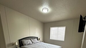 Un dormitorio con cama, mesitas de noche, una ventana y una lámpara en el techo.