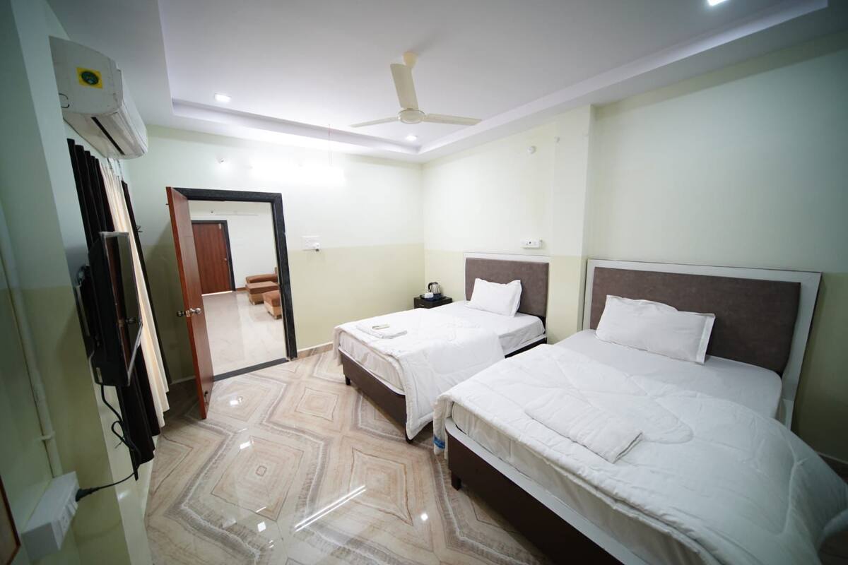 A hotel room with two beds, a ceiling fan, a TV, and a door leading to a hallway.
