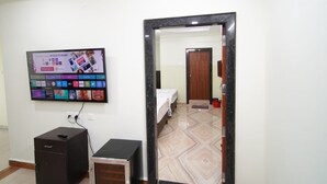 Ett hotellrum med en TV som är monterad på väggen, ett skrivbord, en garderob och en säng.