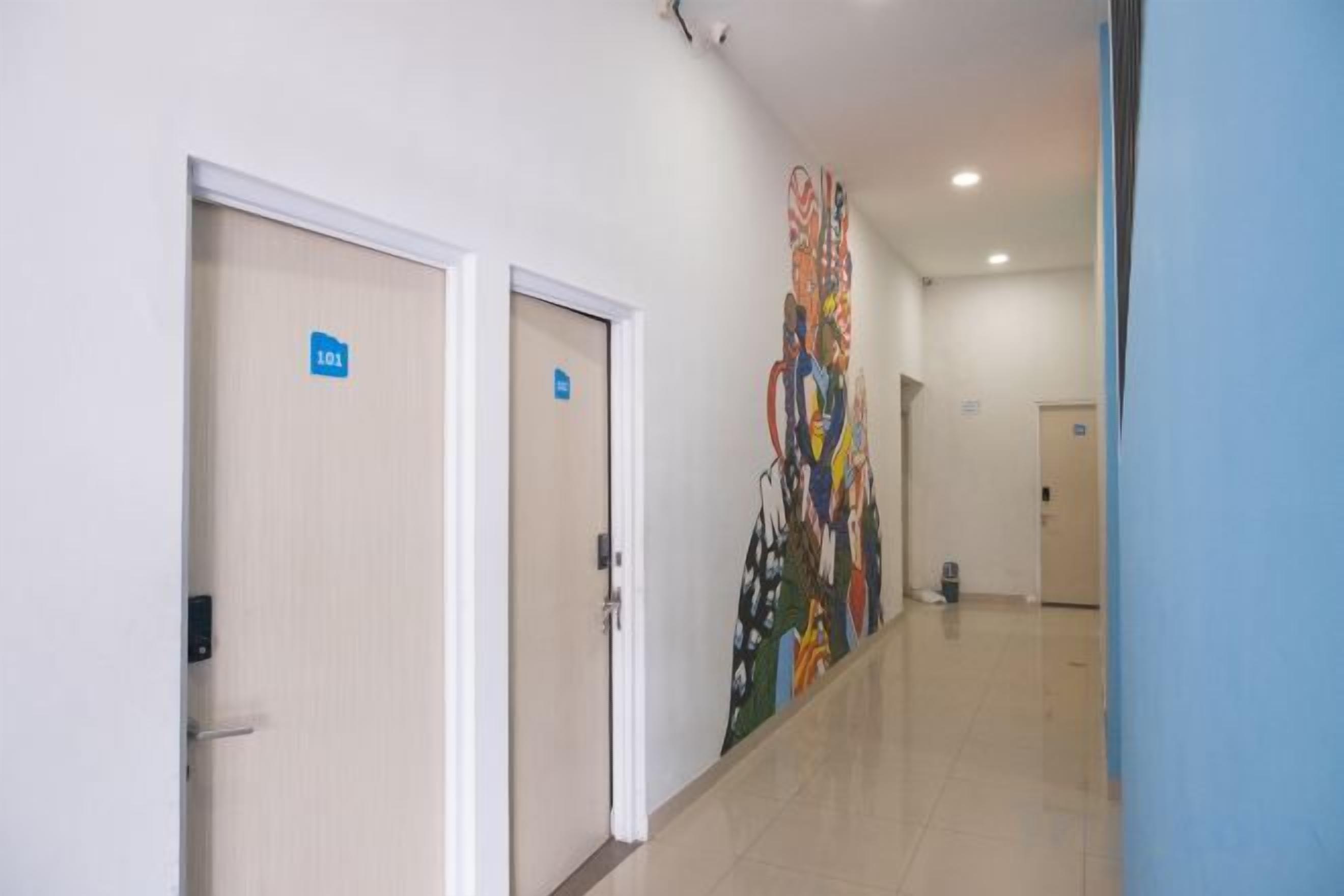 Un pasillo con dos puertas, una señalizada para acceso a habitaciones y otra para un baño. Un mural colorido decora la pared.