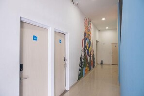 Un couloir avec deux portes, dont une indique l’accès à une pièce et l’autre à une salle de bain. Un mur est décoré d’une fresque colorée.