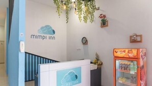 A reception area with a white reception desk, a clock, and a Coca-Cola refrigerator. - INNCA Telaga Bodas, Semarang (Gajahmungkur)