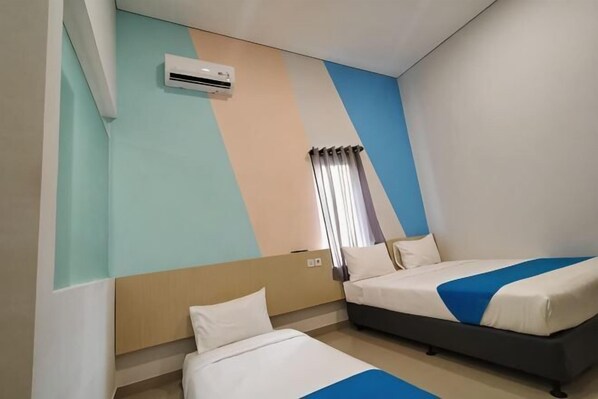 Una habitación de hotel con dos camas, una ventana con cortinas, un equipo de aire acondicionado y una pared con diseño geométrico.
