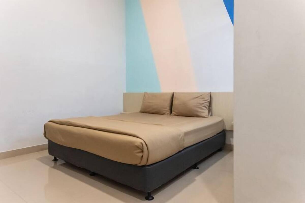 Un lit avec un cadre foncé et une literie beige, dans une pièce aux murs blancs et à un mur d’accent bleu.
