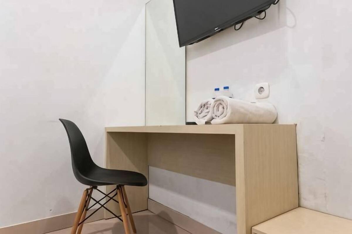 Une chambre d’angle avec un bureau en bois, une chaise noire, un téléviseur fixé au mur et une serviette posée sur le bureau.