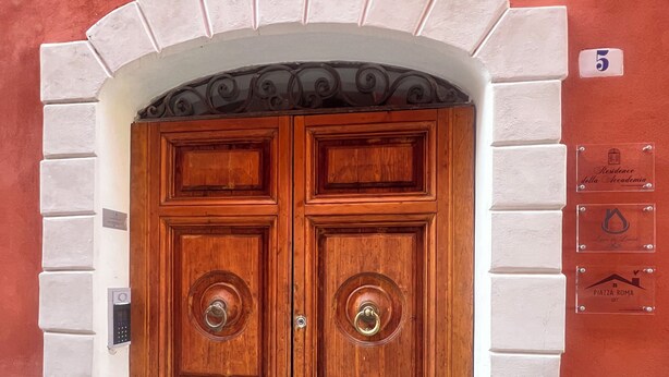 A double wooden door with a metal handle, set in a white brick archway. - Lovoleti Lodge (Modena)