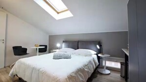 A modern bedroom with a skylight, a bed with white bedding, a bedside table, a chair, and a small round table with a lamp. - Lovoleti Lodge (Modena)