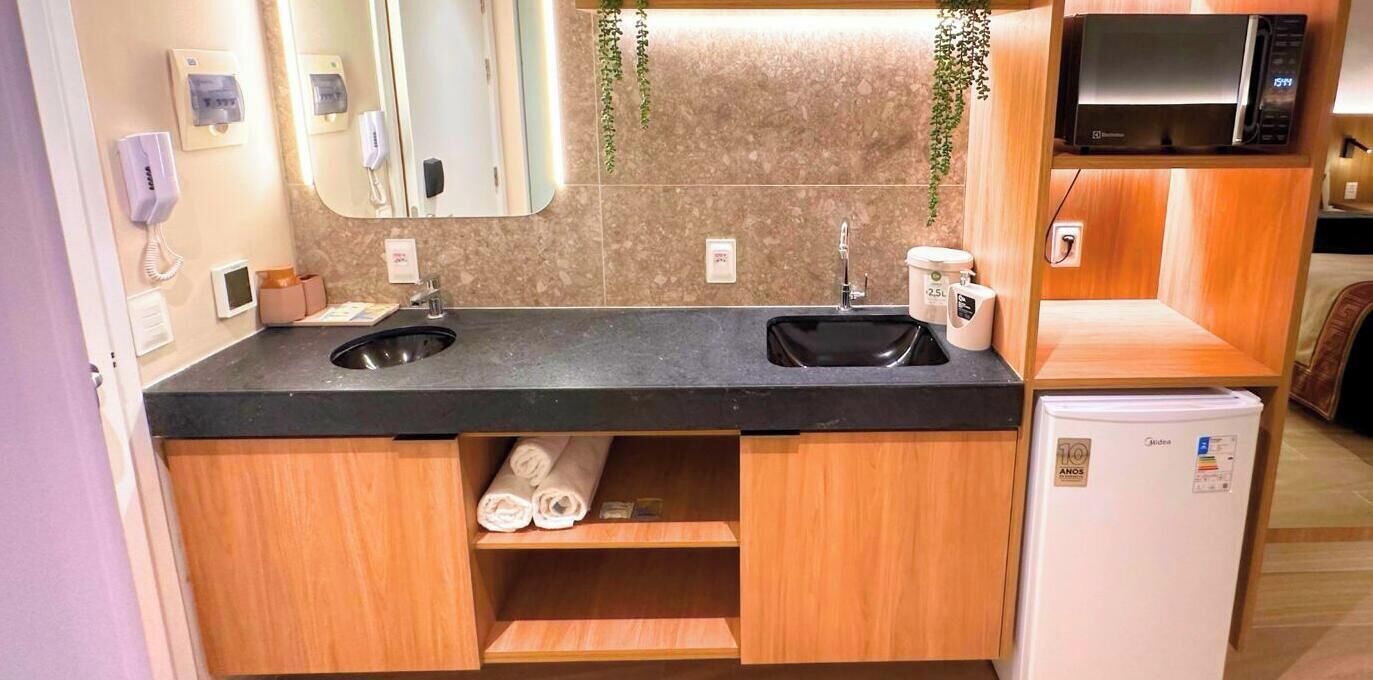 Un bany modern amb un lavabo doble, un mirall, una barra de tovalloles, un frigorífic petit i una televisió.