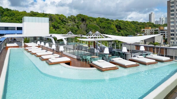 A rooftop pool area with sun loungers and umbrellas, surrounded by buildings and greenery. - Setai Yacht Apart - Hotel by Lesuites (João Pessoa)