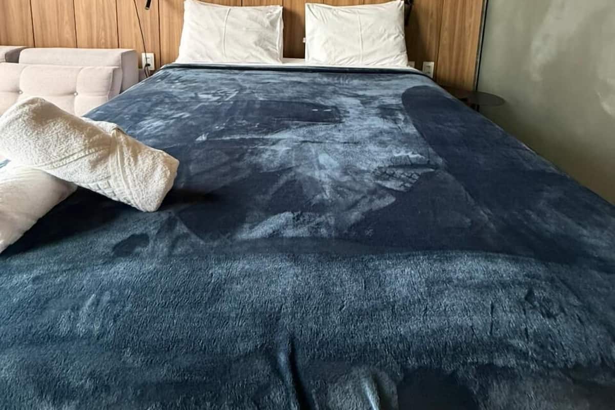 A modern bedroom with a wooden panel wall, a large bed with a blue textured bedspread, white pillows, and a white bedside table.