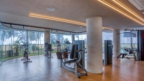 A modern gym with various exercise equipment, large windows, and a view of palm trees. - Setai Yacht Apart - Hotel by Lesuites (João Pessoa)