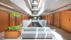 A modern hotel lobby with a central staircase, wooden paneling, and a seating area with a plant and a sofa. - Setai Yacht Apart - Hotel by Lesuites (João Pessoa)