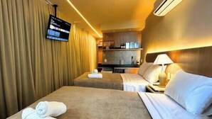 A hotel room with two beds, a TV mounted on the wall, and a kitchenette in the background. - Setai Yacht Apart - Hotel by Lesuites (João Pessoa)