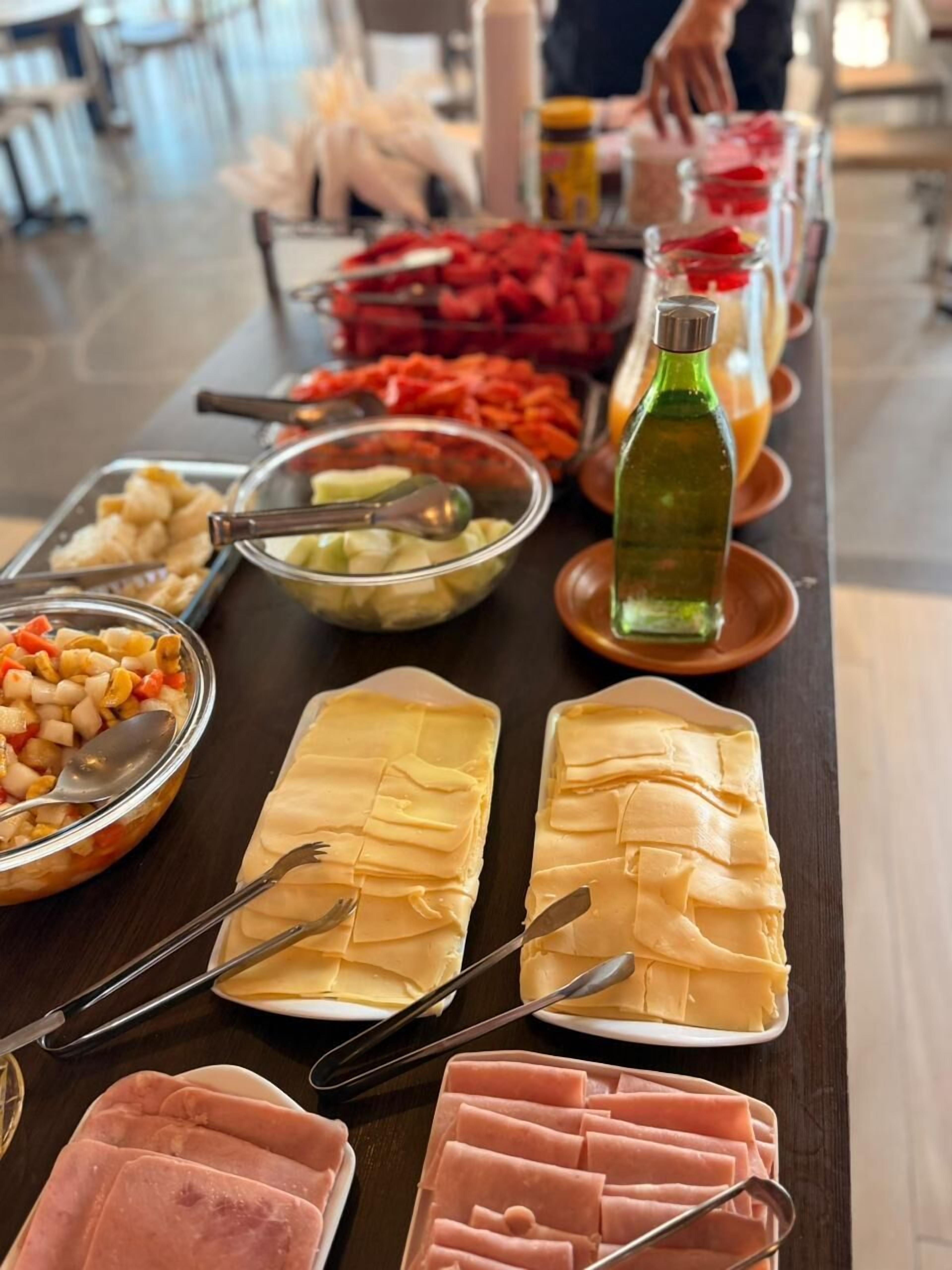 Una mesa de buffet con diversos alimentos, incluyendo carnes en rodajas, verduras y una botella de aceite.