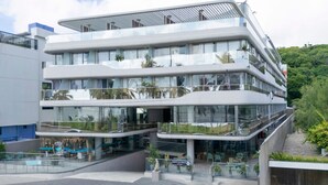 A modern multi-story hotel with a glass facade, outdoor seating, and a sign indicating public access. - Setai Yacht Apart - Hotel by Lesuites (João Pessoa)