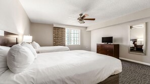 Habitación de hotel con dos camas, ventilador de techo, televisión, cómoda y un espejo grande.