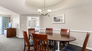 Un comedor con una mesa redonda, sillas de madera, una araña y un cuadro en la pared.