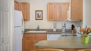 Eine Küche mit Holzschränken, einem weißen Kühlschrank, einer Spüle, einem Geschirrspüler, einer Kaffeemaschine und einem Mixer.