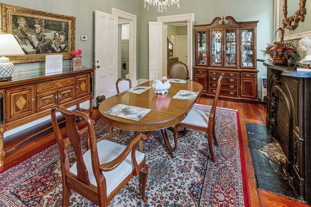 A formal dining room with a wooden table, chairs, and a patterned rug.