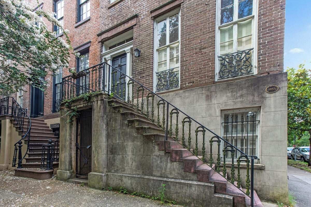 Un immeuble à plusieurs étages, construit en briques, avec un escalier en pierre menant à l’entrée.