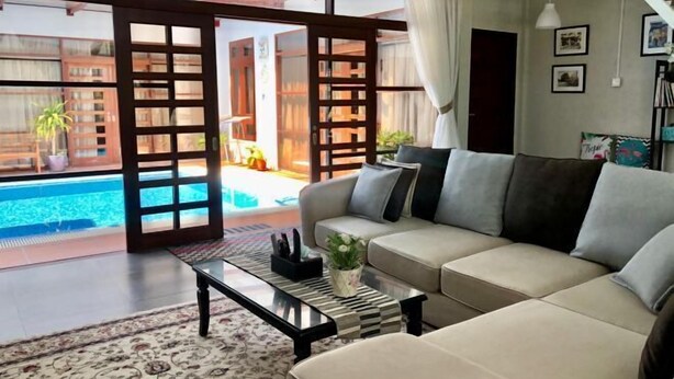 A living room with a beige sofa, a patterned coffee table, and a view of a swimming pool through open doors. - Casa Tanjung Jara (Kuala Dungun)