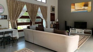 A living room with a sofa, dining table, chairs, a TV, and artwork on the wall. - Casa Tanjung Jara (Kuala Dungun)