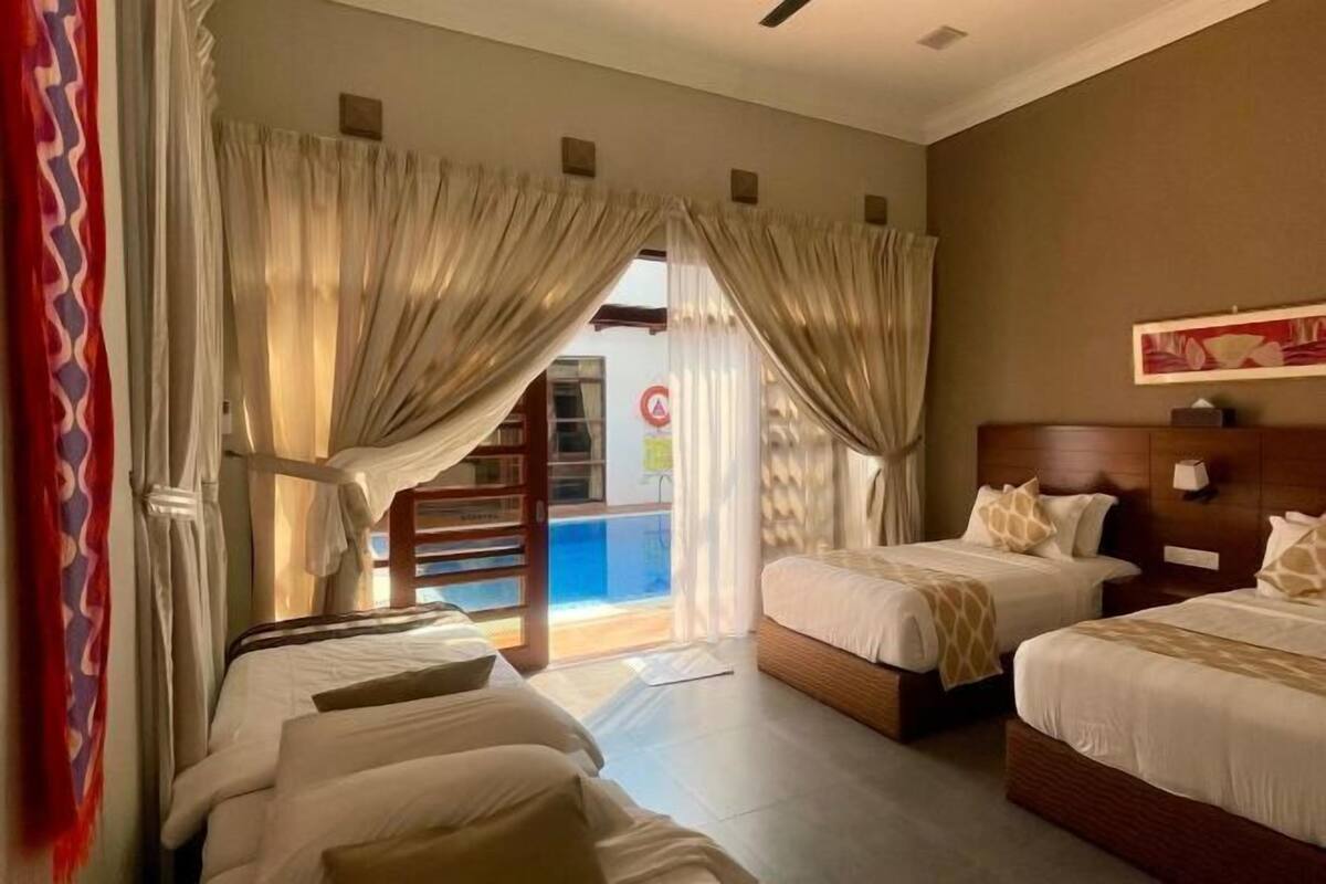 Habitación de hotel con dos camas, cabecera de madera y vista a una piscina a través de una puerta de vidrio.