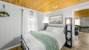 A bedroom with a wooden ceiling, white walls, a bed with a green blanket, a bedside lamp, and a painting. - Summer Sale! Country Guesthouse near Waterparks and Birch Run Outlets (Bridgeport)