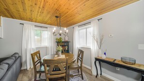 A dining area with a wooden table, four chairs, a chandelier, and a side table with decorative items. - Summer Sale! Country Guesthouse near Waterparks and Birch Run Outlets (Bridgeport)