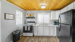 A kitchen with white cabinets, a black refrigerator, a stove, and a trash can. - Summer Sale! Country Guesthouse near Waterparks and Birch Run Outlets (Bridgeport)