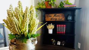 A dining table with a woven placemat, a metal pitcher with flowers, a wooden sign with the text "Live More Worry Less", and a black shelf with books and decorative items. - Summer Sale! Country Guesthouse near Waterparks and Birch Run Outlets (Bridgeport)