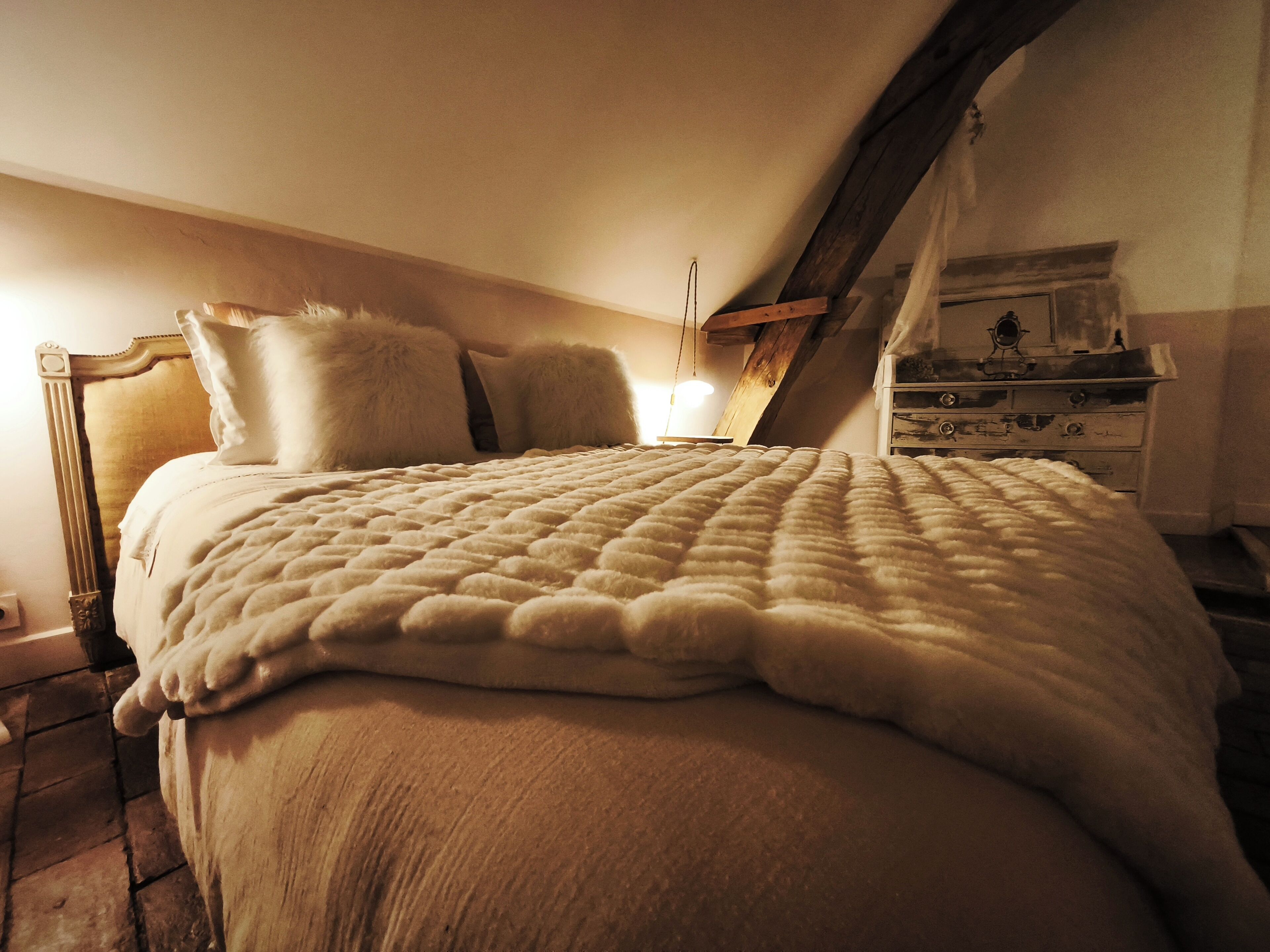 A cozy bedroom with a large bed, a wooden headboard, and a dresser with drawers.