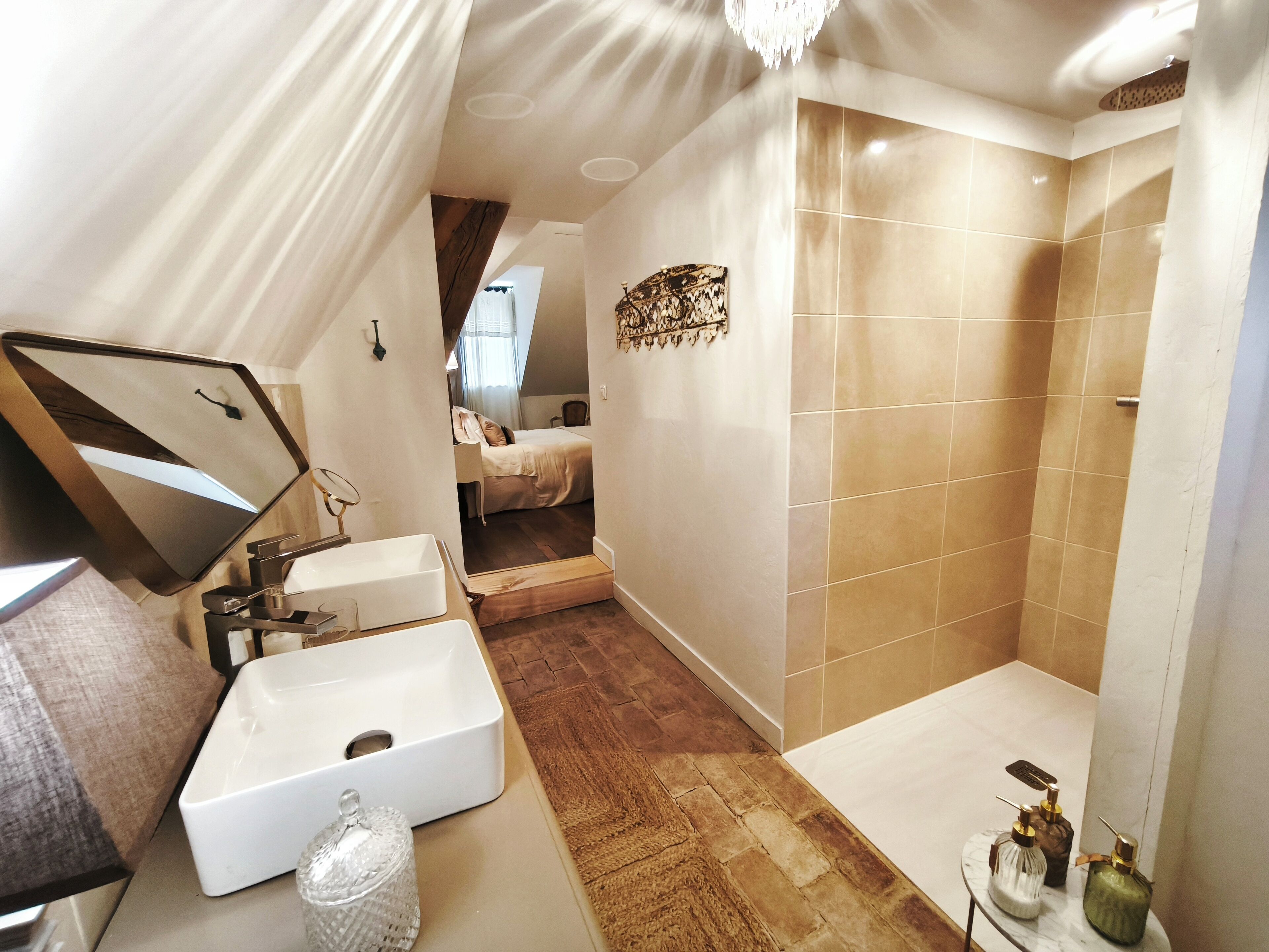 A modern bathroom with a large mirror, two sinks, a shower, and a small vanity table with toiletries.