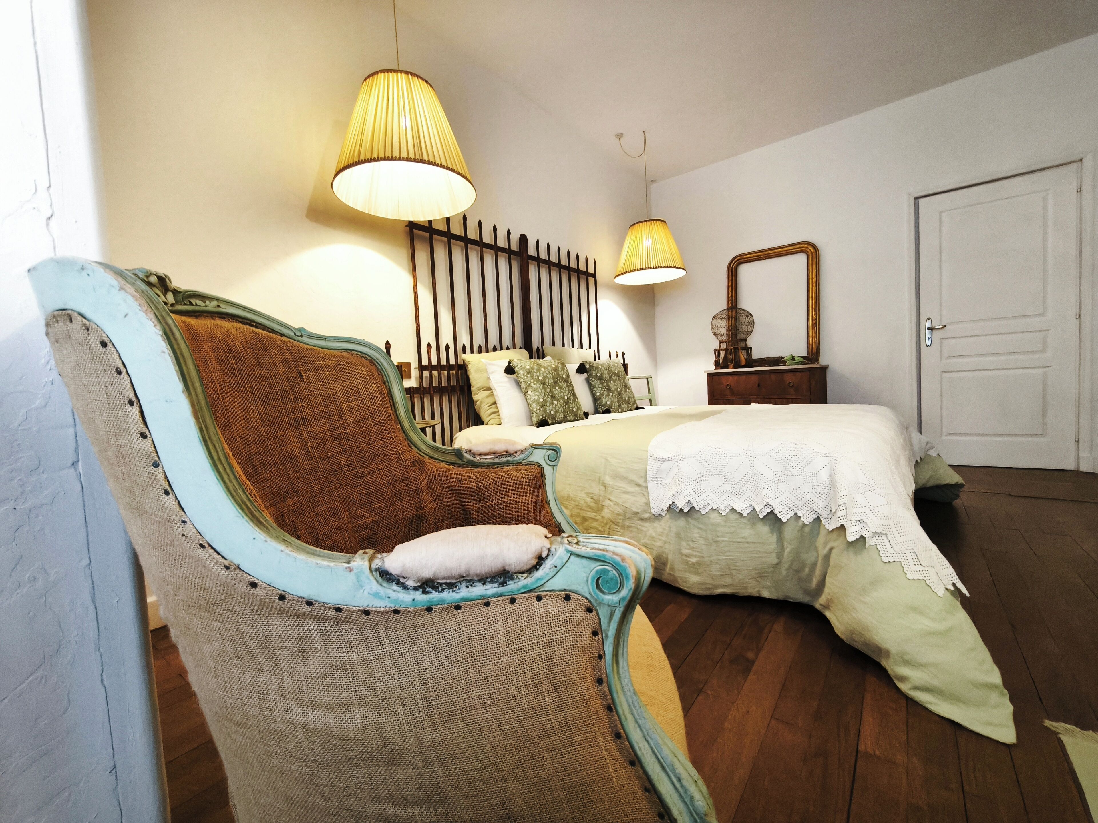 Un dormitorio con cama, una silla, dos lámparas, un espejo y una puerta.