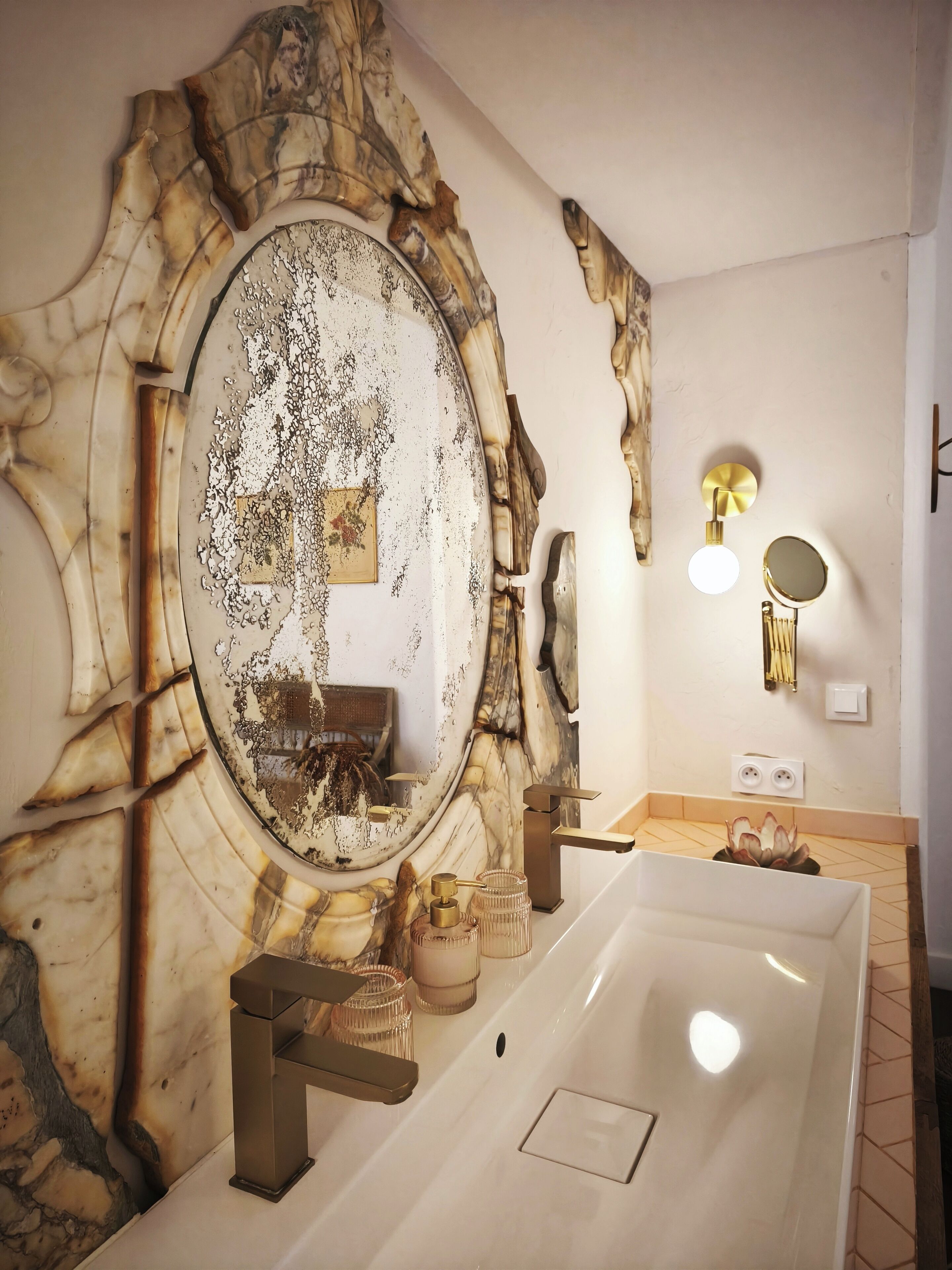 Un baño con tocador de mármol, un espejo grande e instalaciones doradas.
