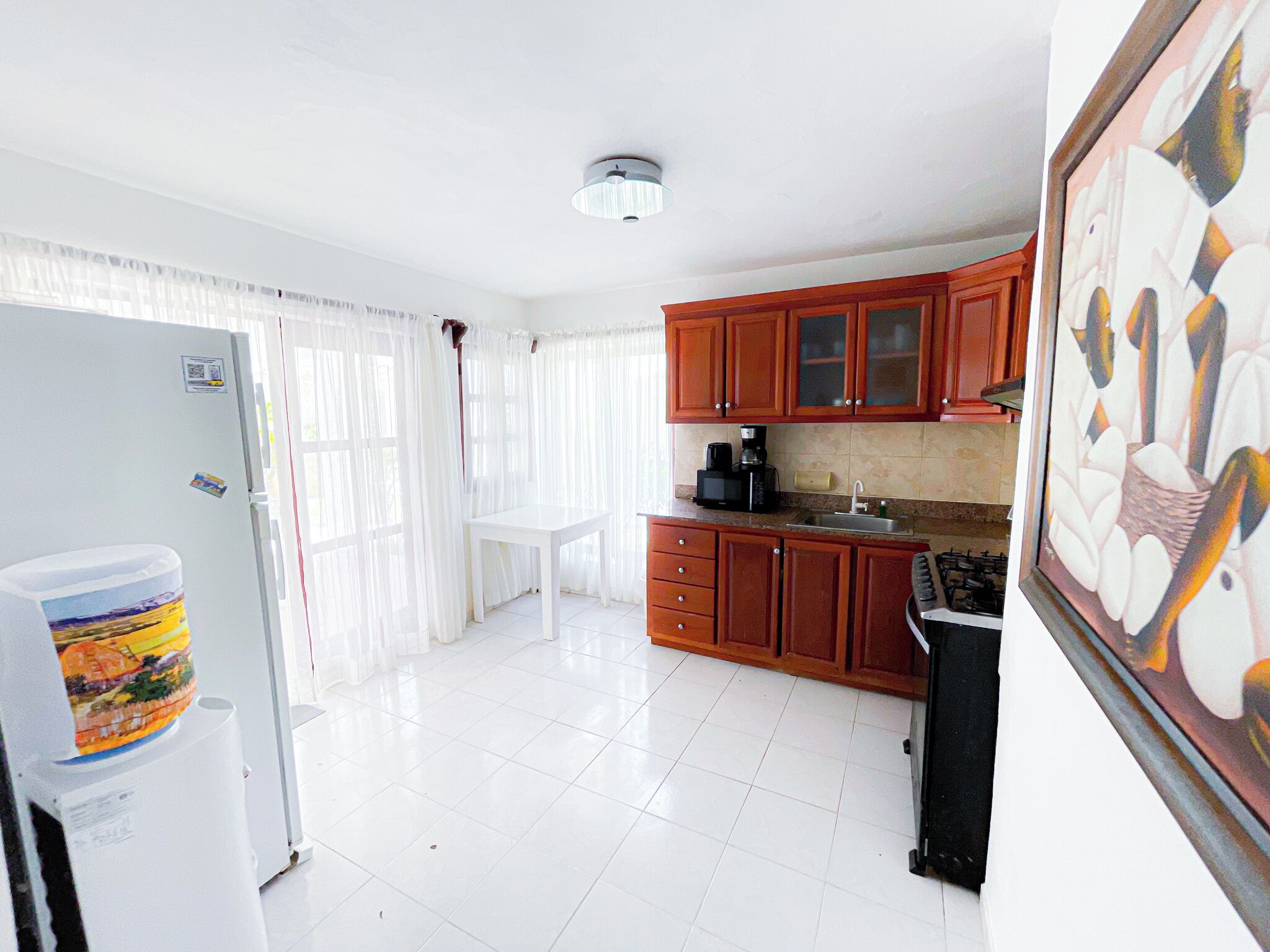 A compact kitchen with white cabinets, a refrigerator, a coffee maker, and a sink.