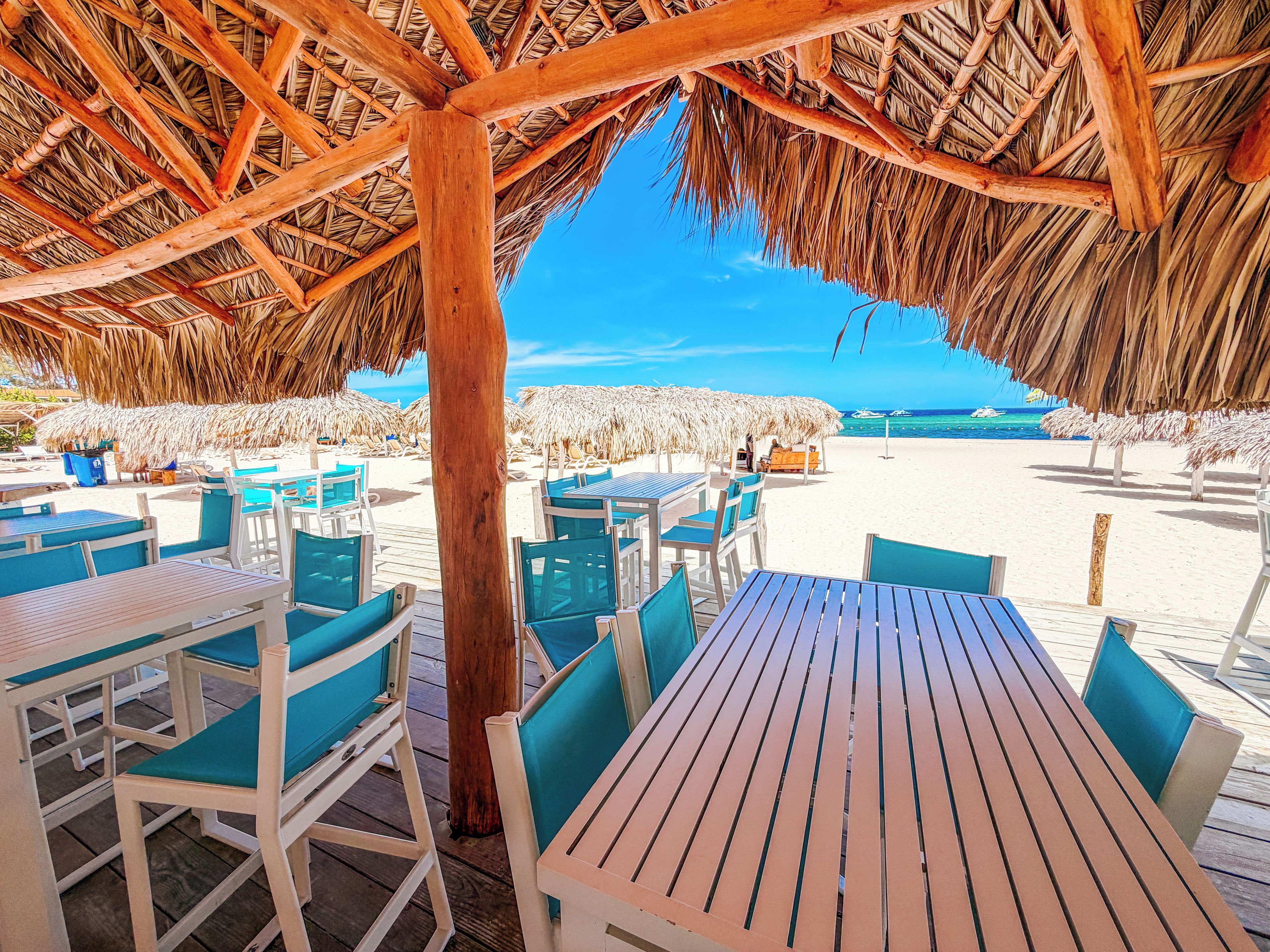 Un espace extérieur aménagé avec des tables et des chaises en bois, un toit de chaume et une vue sur la plage.