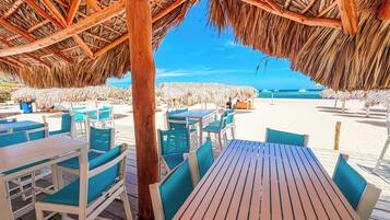 Un espace extérieur aménagé avec des tables et des chaises en bois, un toit de chaume et une vue sur la plage.