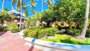 Um resort tropical com uma trilha sinuosa, palmeiras e um edifício com telhado de palha.