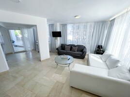 Ein modernes Wohnzimmer mit einem weißen Sofa, einem grauen Sofa, einem Glastisch und einem flachbildfernseher, der an der Wand befestigt ist.