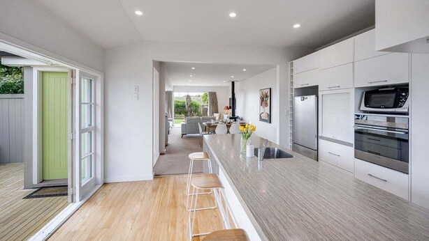 A modern kitchen with a central island, stainless steel appliances, and a view to the outdoor area. - 7th Heaven (Napier)