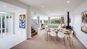 A spacious dining area with a high ceiling, a staircase leading to a balcony, and a view of the outdoors. - 7th Heaven (Napier)