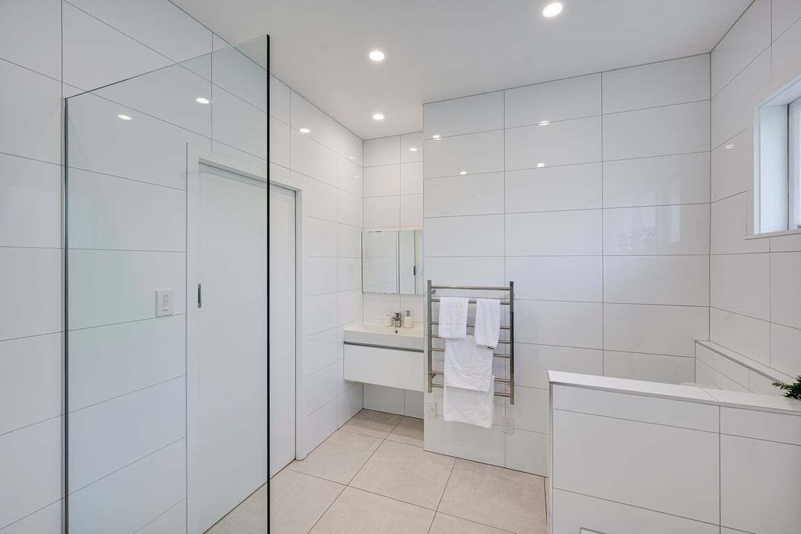 A modern bathroom with a glass shower enclosure, a white vanity with a mirror, and a towel rack.