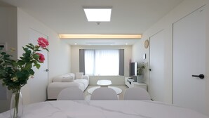 Et moderne hotelværelse med et marmorbord, en hvid sofa, et fladskærms-tv og et stort vindue med gardiner.