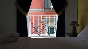 Een hotelkamer met een bed, een nachtkastje met lamp, en uitzicht op een balkon met een tafel en stoelen.