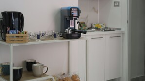 Een kitchenette met een koffiezetapparaat, kopjes en een broodmand.