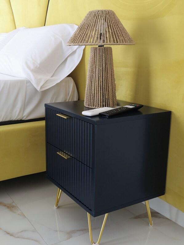 A modern bedroom with a yellow headboard, a dark blue nightstand with gold legs, and a textured lamp.