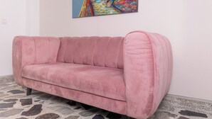 Un canapé rose dans une pièce dont le sol est recouvert de carreaux et où l’on peut voir un tableau coloré accroché au mur.